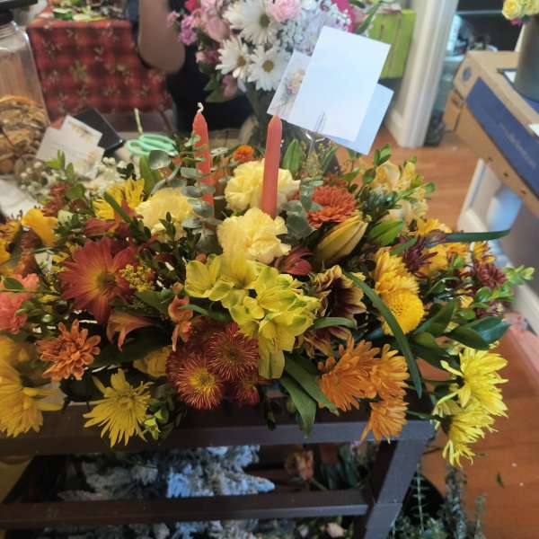 Mixed bouquet with yellow, orange, and red flowers arranged around two candles