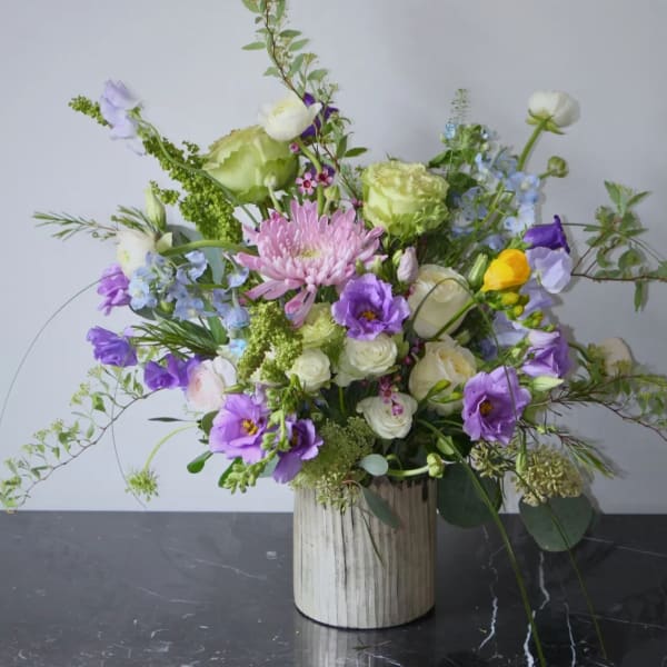 Mixed floral arrangement in a ribbed white vase with purple, white, and green blooms