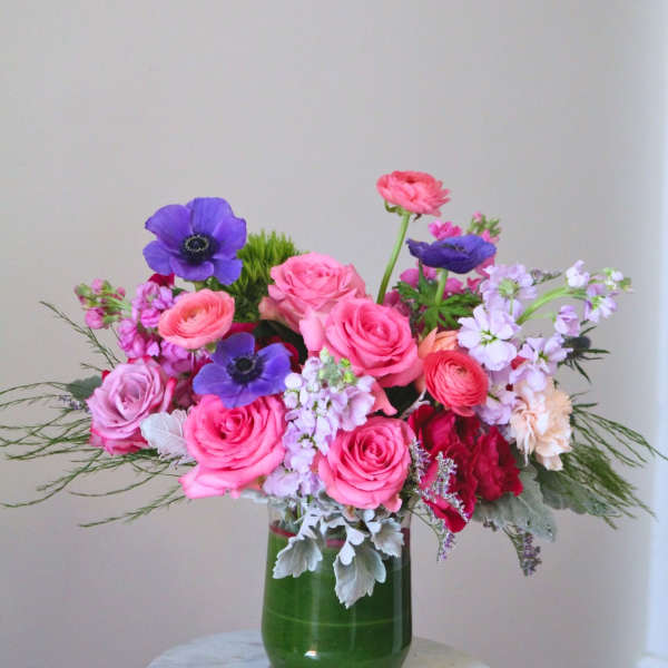 Pink and purple mixed flower arrangement in a green glass vase