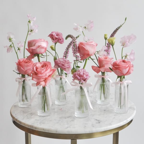 Pink roses and carnations in small glass vases with ribbon ties