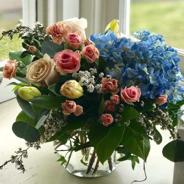 Bouquet of pink and cream roses with blue hydrangeas in a glass vase