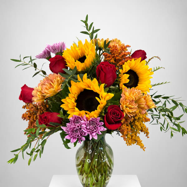 Bouquet of sunflowers, red roses, and purple mums in a glass vase