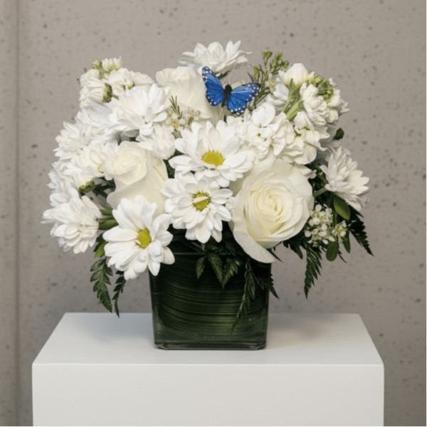 White flowers arranged in a square glass vase with a blue butterfly accent.