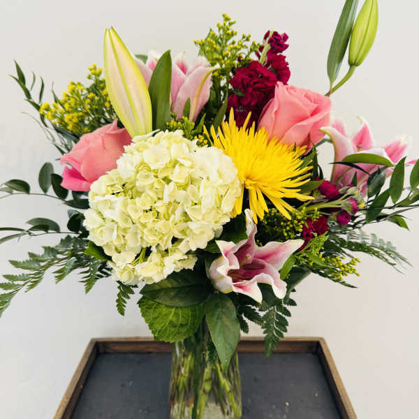 Mixed bouquet in a glass vase with pink roses, lilies, hydrangea, and yellow blooms