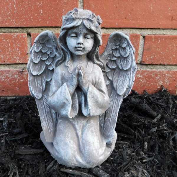 Stone angel statue kneeling with folded hands against a brick wall