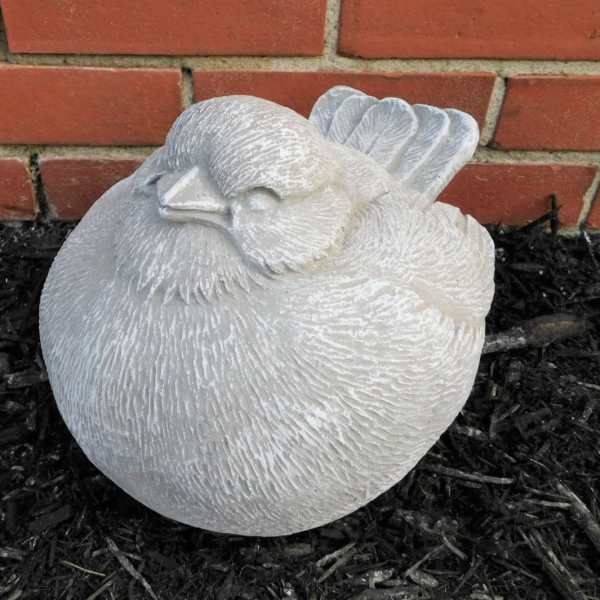 White bird-shaped garden statue resting on dark mulch in front of a brick wall