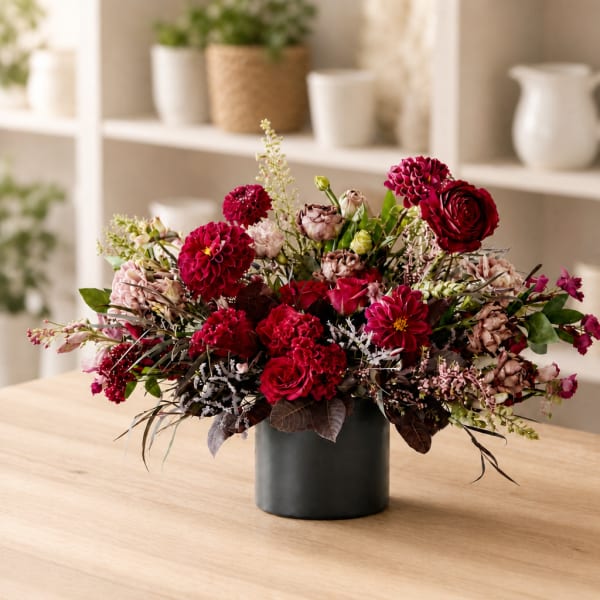Red and pink floral arrangement in a black vase on a table
