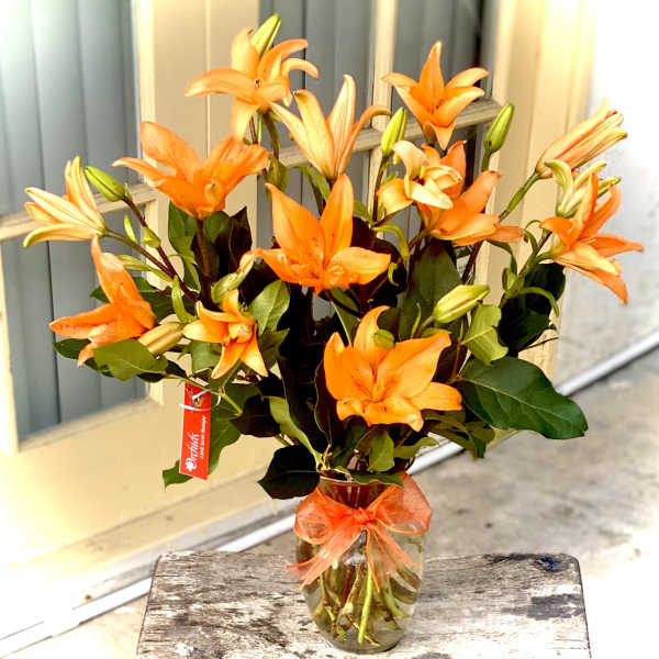 Orange lilies in a glass vase with a ribbon bow