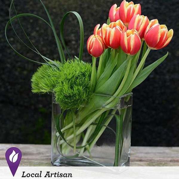 Pink and yellow tulips in a clear glass vase with green decorative accents