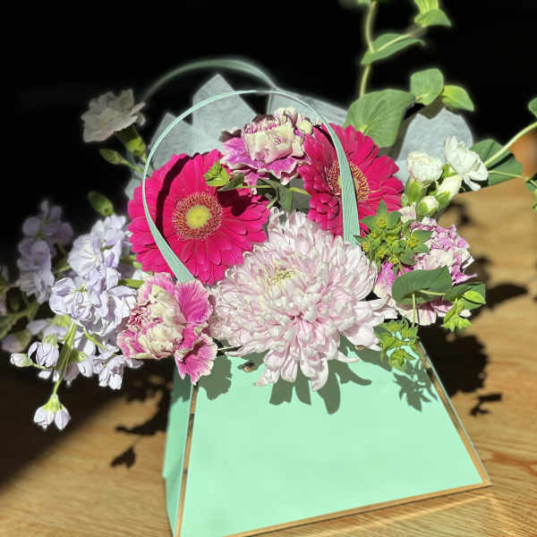 Pink and white flowers arranged in a mint green handled box