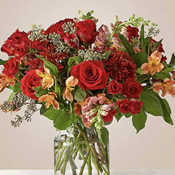 Red roses and mixed blooms arranged in a clear glass vase