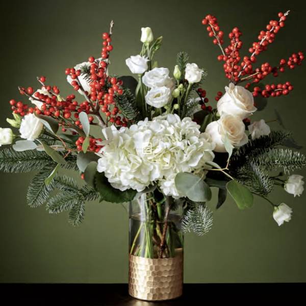 White flowers and red berry branches in a glass vase with a gold base
