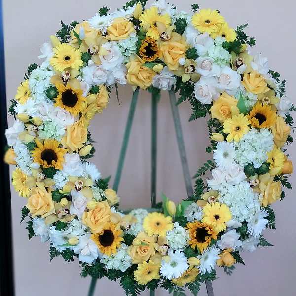 Circular floral wreath with yellow and white flowers on a stand