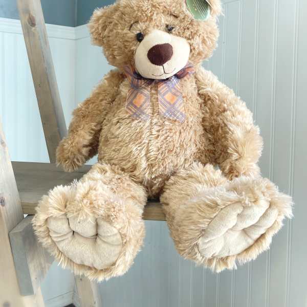 Large plush teddy bear with a plaid bow sitting on a wooden ladder
