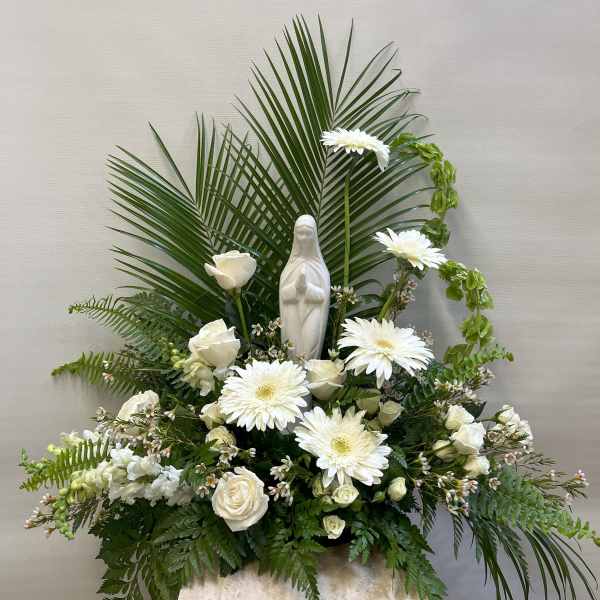 White floral arrangement with a small statue of the Virgin Mary