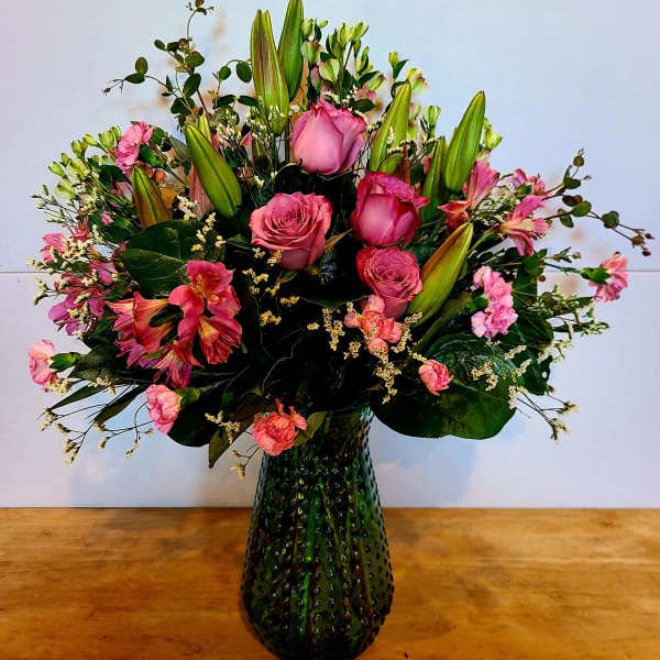 Pink roses and lilies arranged in a green glass vase