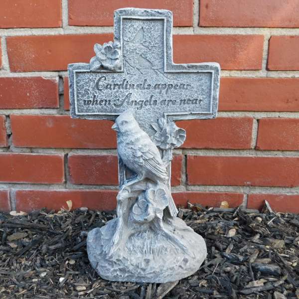 Stone memorial cross with a bird and floral relief against a brick wall