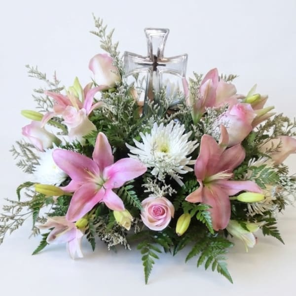Pink lilies and white flowers arranged around a clear glass cross