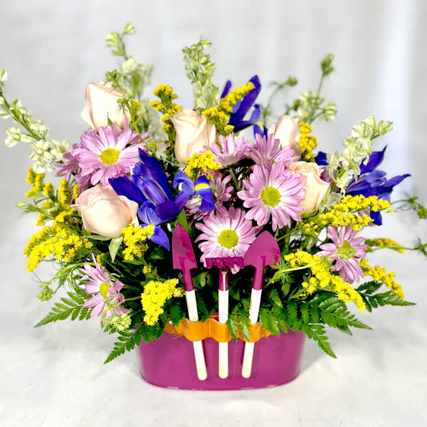 Mixed bouquet in a pink container with small garden tools