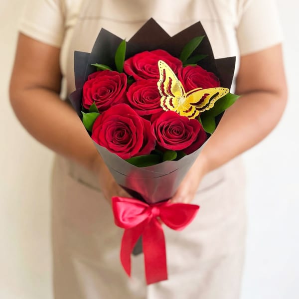 Bouquet of red roses wrapped in black paper with a red ribbon and butterfly decoration