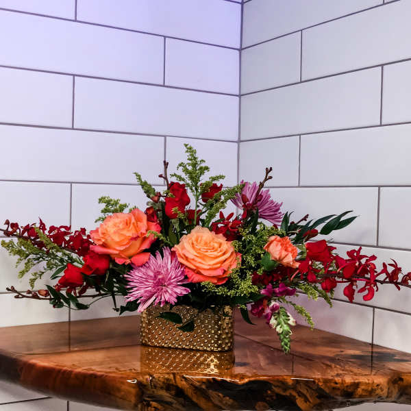 Mixed bouquet of roses and purple blooms in a gold vase