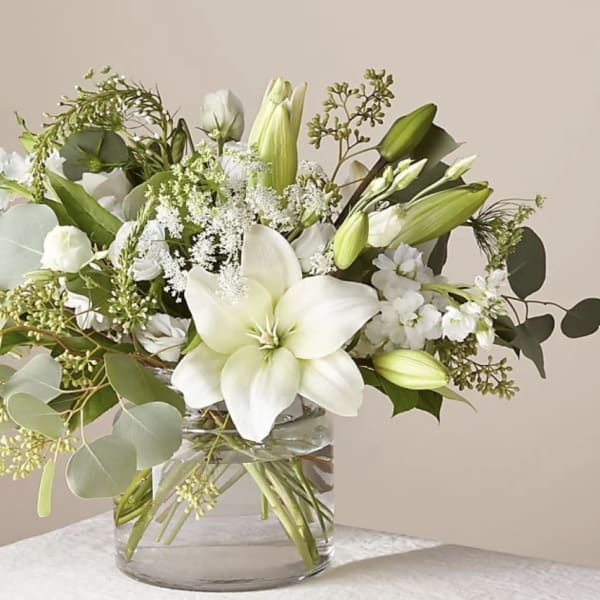 White lilies and greenery arranged in a clear glass vase