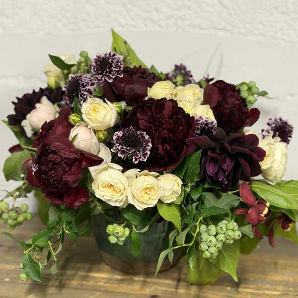 Bouquet of burgundy and cream roses with dark blooms in a vase