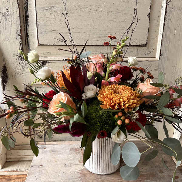 Mixed bouquet in a white ribbed vase with peach, red, and white blooms