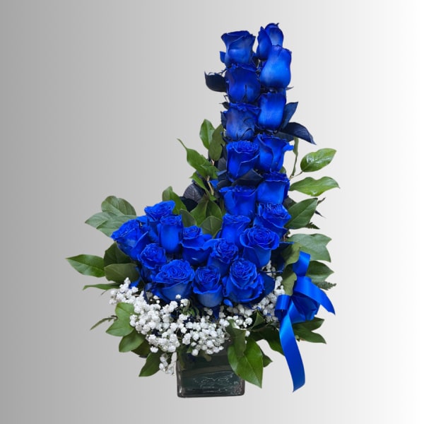 Blue roses arranged in a square glass vase with white filler flowers