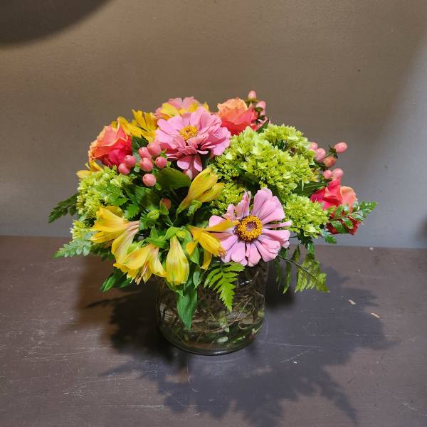 Mixed pink and yellow flowers arranged in a glass vase