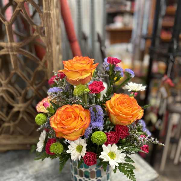 Bright mixed bouquet with orange roses in a mosaic vase