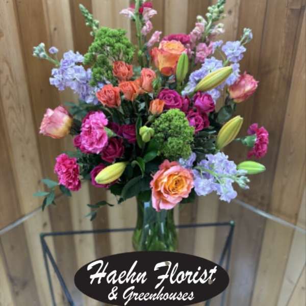 Tall mixed bouquet in a glass vase with pink, orange, and lavender flowers