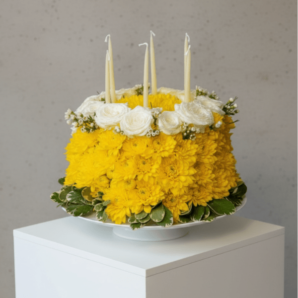 Yellow and white floral cake with four taper candles on a white pedestal