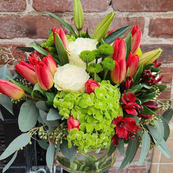 Mixed arrangement of red tulips, white roses, green hydrangeas and lilies in a clear glass vase