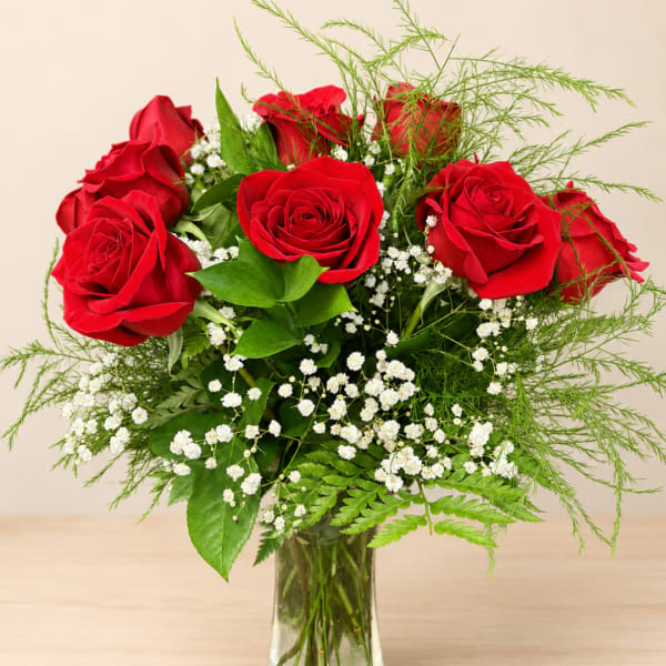 Red roses arranged in a clear glass vase with white filler flowers
