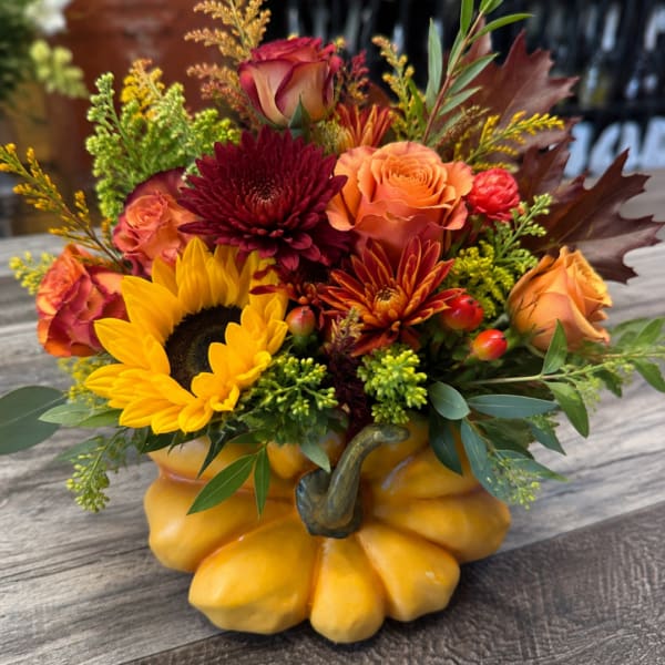 Fall floral arrangement in a pumpkin-shaped container with sunflowers and roses