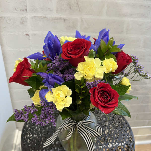 Bouquet of red roses, yellow carnations, and purple flowers in a glass vase