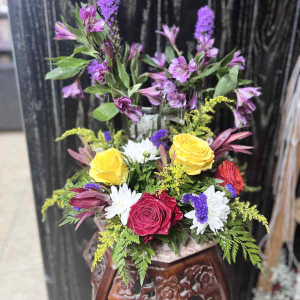 Mixed bouquet with yellow and red roses, white daisies, and purple flowers in a vase