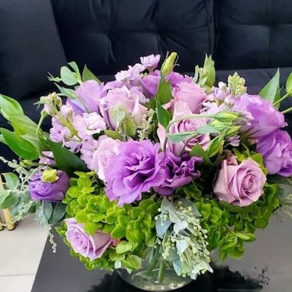 Low round arrangement of purple and lavender flowers in a clear glass bowl vase