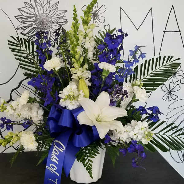 White and blue floral arrangement in a white vase with a blue ribbon