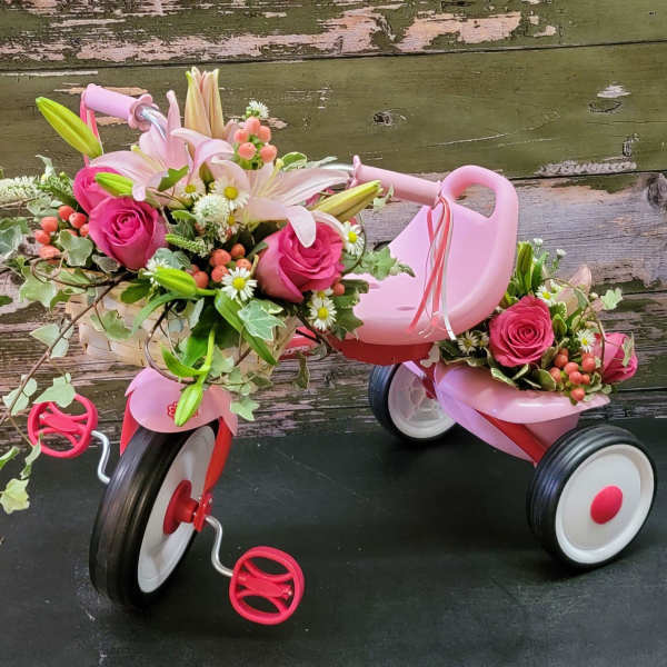 Pink floral arrangements on a small tricycle with white lilies and roses