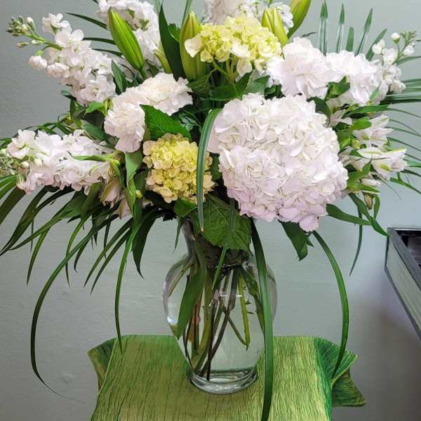 White floral arrangement in a clear glass vase with long green leaves