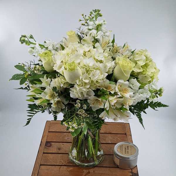 White floral arrangement in a clear glass vase with a small candle beside it