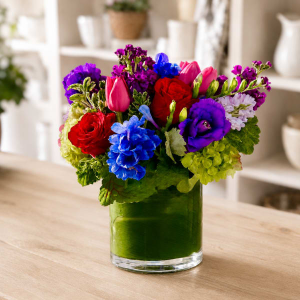 Colorful bouquet of roses, tulips, and purple blooms in a glass vase