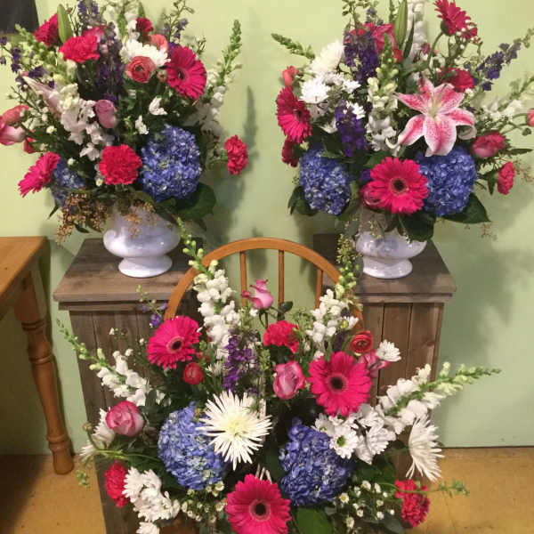 Three colorful floral arrangements with gerbera daisies and hydrangeas in white vases