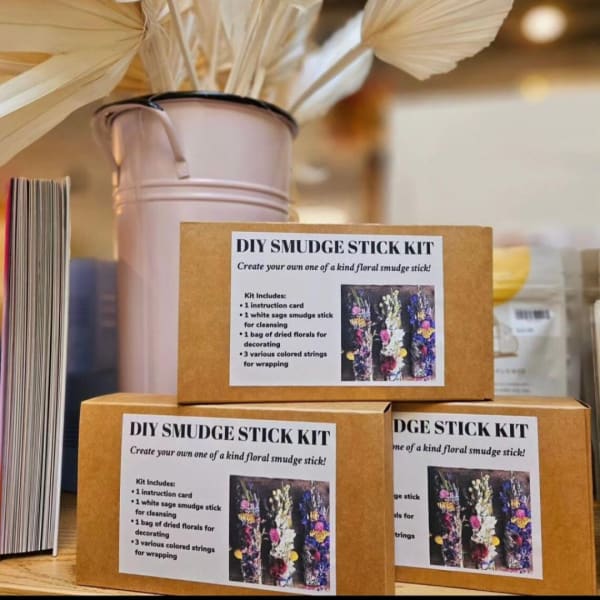 DIY smudge stick kits stacked beside a pale vase with dried leaves.