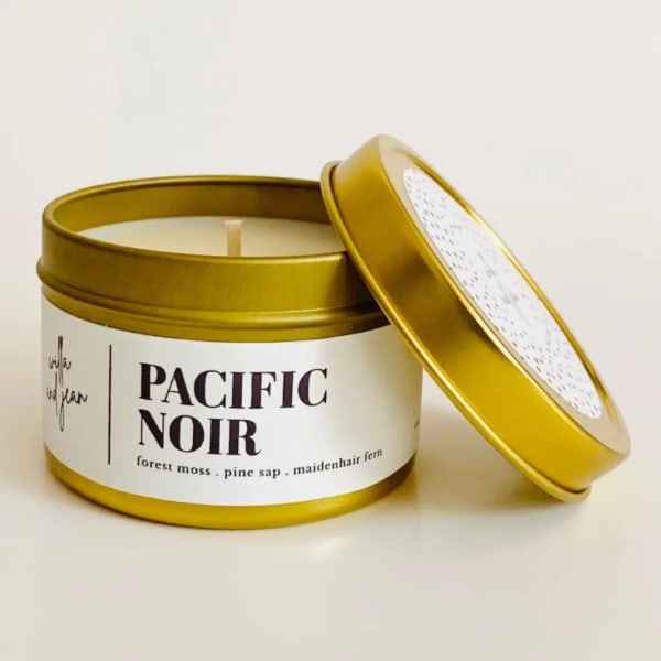 Gold tin candle labeled Pacific Noir with lid leaning beside it