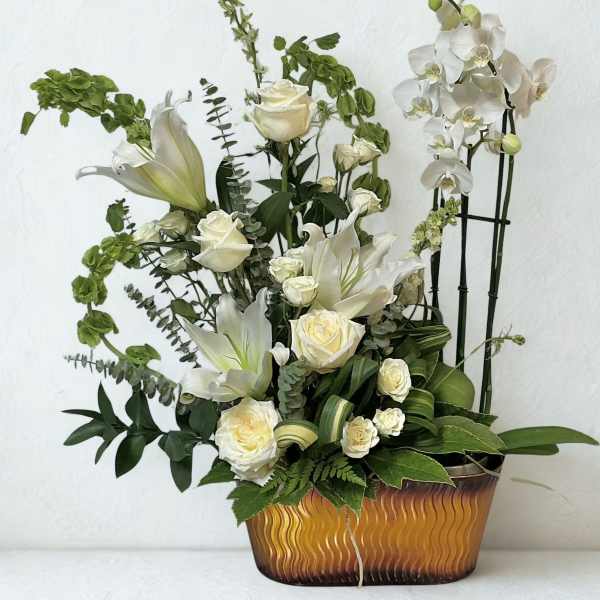 White roses and lilies arranged in a gold-toned container with orchids.