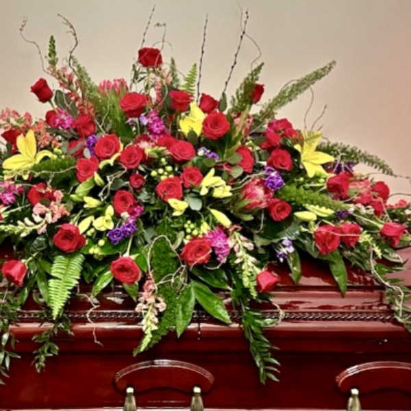 Large red and yellow floral casket spray on a wooden casket