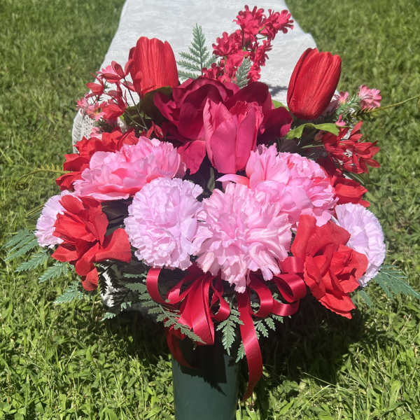 Pink and red floral arrangement in a green vase with a ribbon bow
